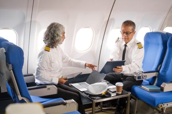 Mature male and female pilots meet inside an airplane, holding hands. Their gesture signifies